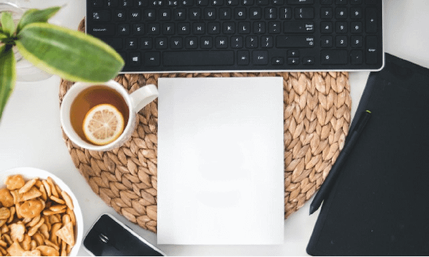A top down picture of a black keyboard at the top with a blank white notepad directly underneath and a latte in a white mug to the left side. Everything is sitting on a circular cork mat. There are some other things that are cut away form the photo. This is used for a health based business article