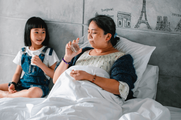 a woman and a child sitting in bed with glasses of water and a white blanket. The woman is actively drinking the water. There are small drawings of different french buildings.
